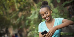 Scenes from urban life in New York City. A young teenage girl sitting on a bench, looking at a pad screen or texting.